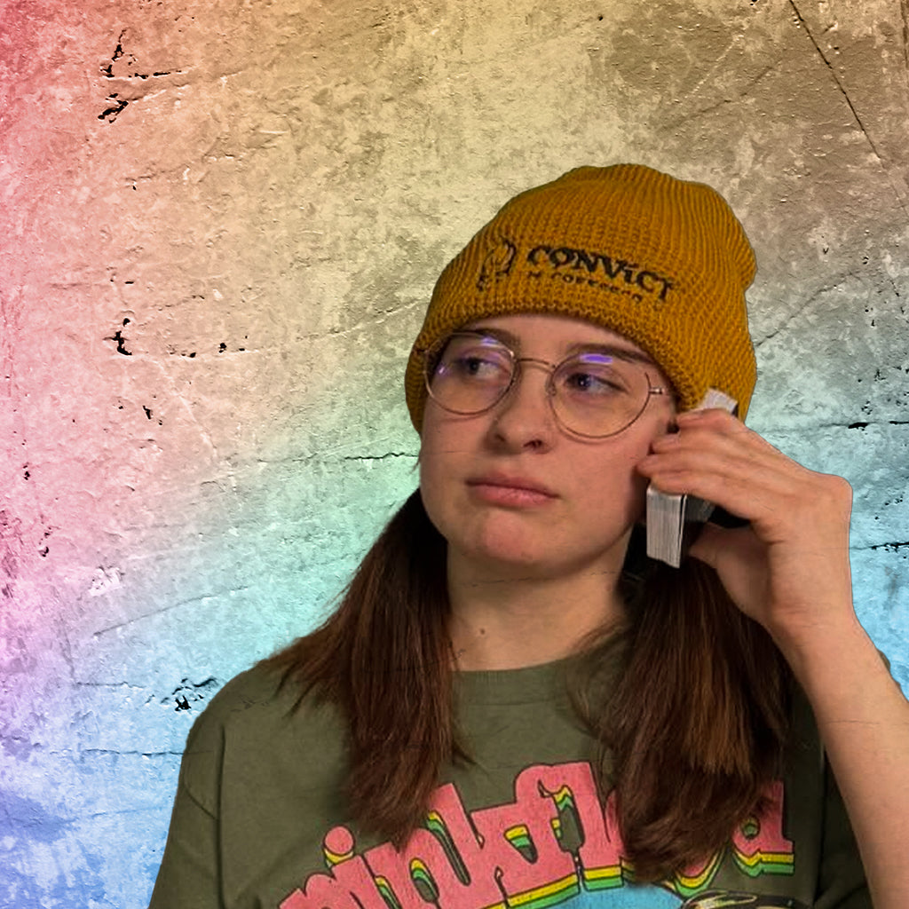 Ava Hendren wearing a yellow beanie and green t-shirt with text, against a textured multicolored background