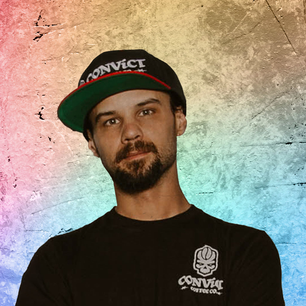 Damien Klehm wearing a black cap and black t-shirt with 'Convict' branding against a colorful textured background