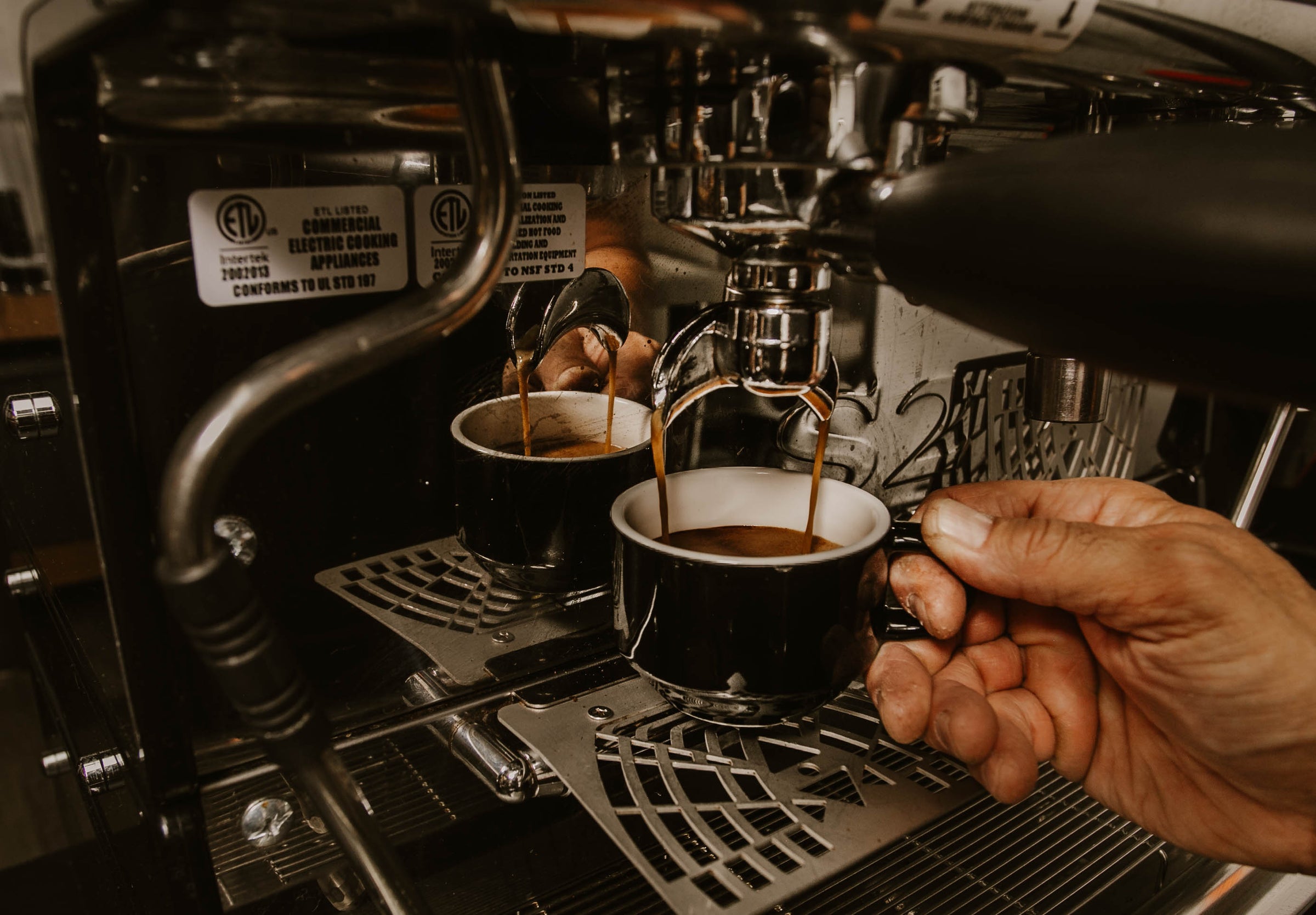 Espresso being poured from a machine into ceramic cup held by a hand.