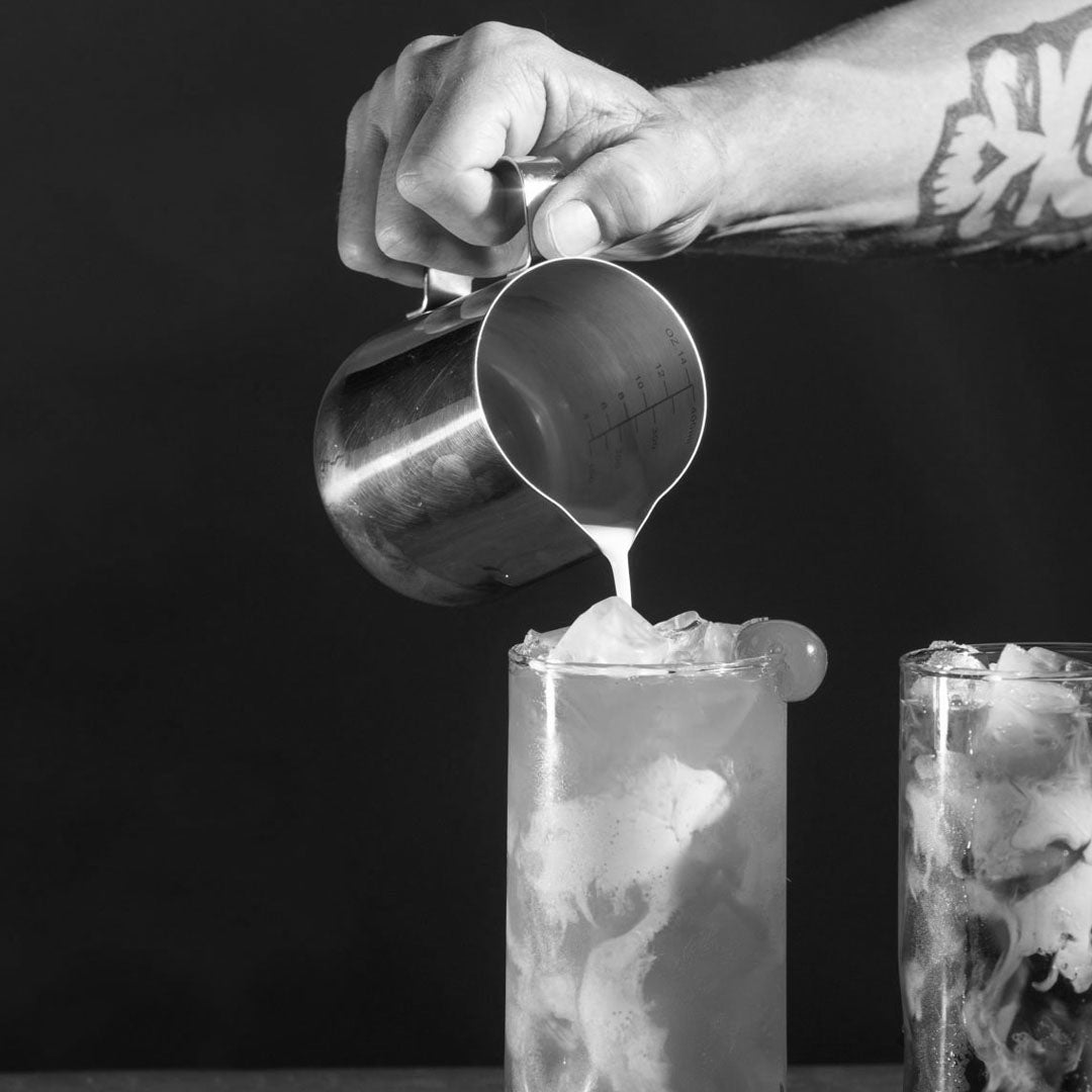 Person pouring a cream into a glass with ice in black and white