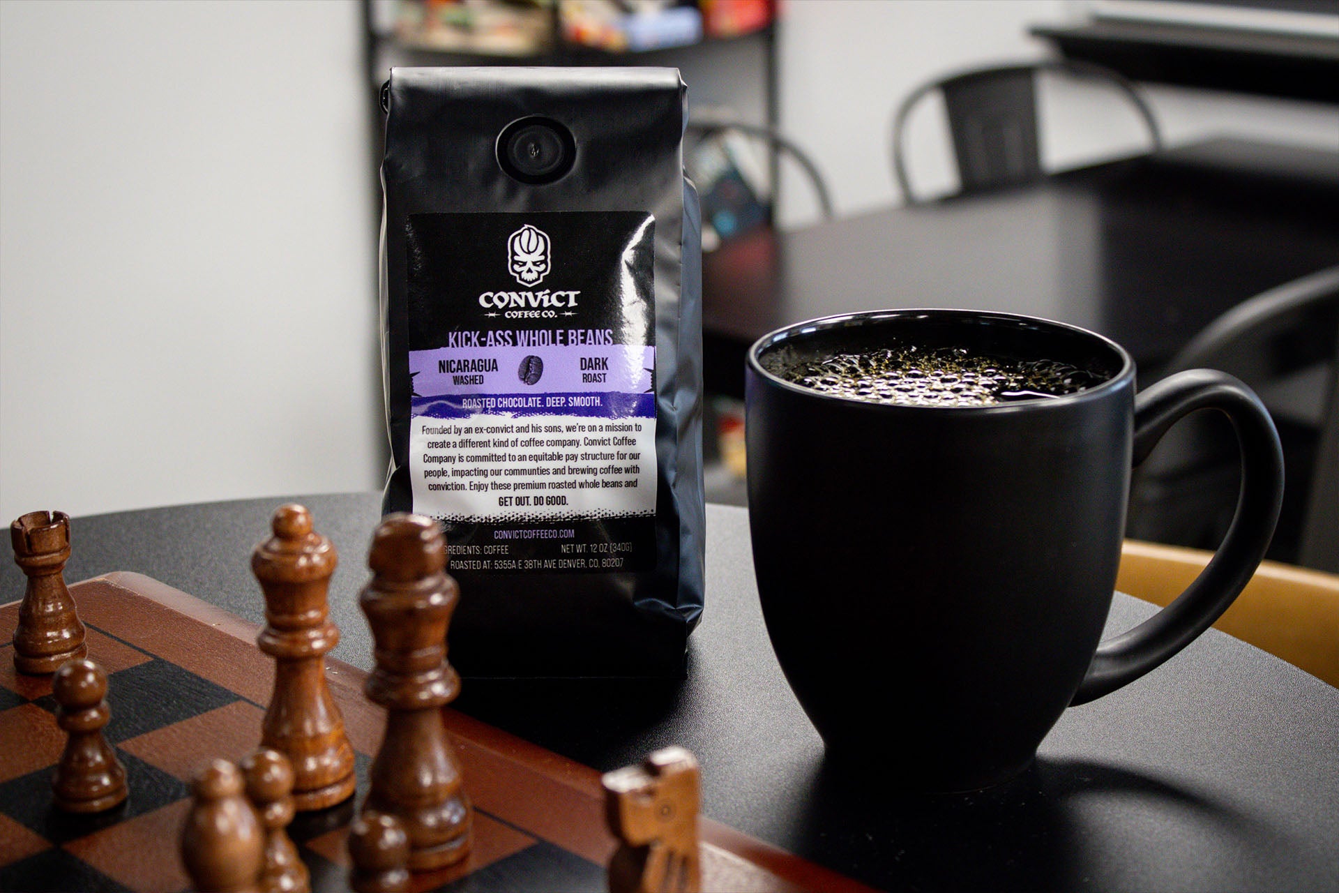 Black coffee mug with a bag of Convict Coffee with a chessboard on a black table