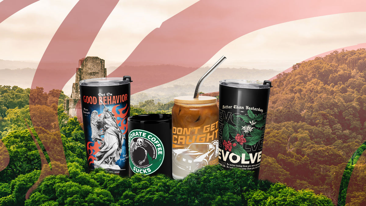 Four novelty tumbler cups arranged together in a stylized outdoor scene with a mountain landscape and red-and-white flag background. The cups include graphic designs: one with a statue and flames reading 'OUT ON GOOD BEHAVIOR,' one black with a skull logo and the words 'CONVICT COFFEE SUCKS,' one amber drink with orange text reading 'DON'T GET CAUGHT,' and one black cup with white text and botanical artwork reading 'Better Than Yesterday.