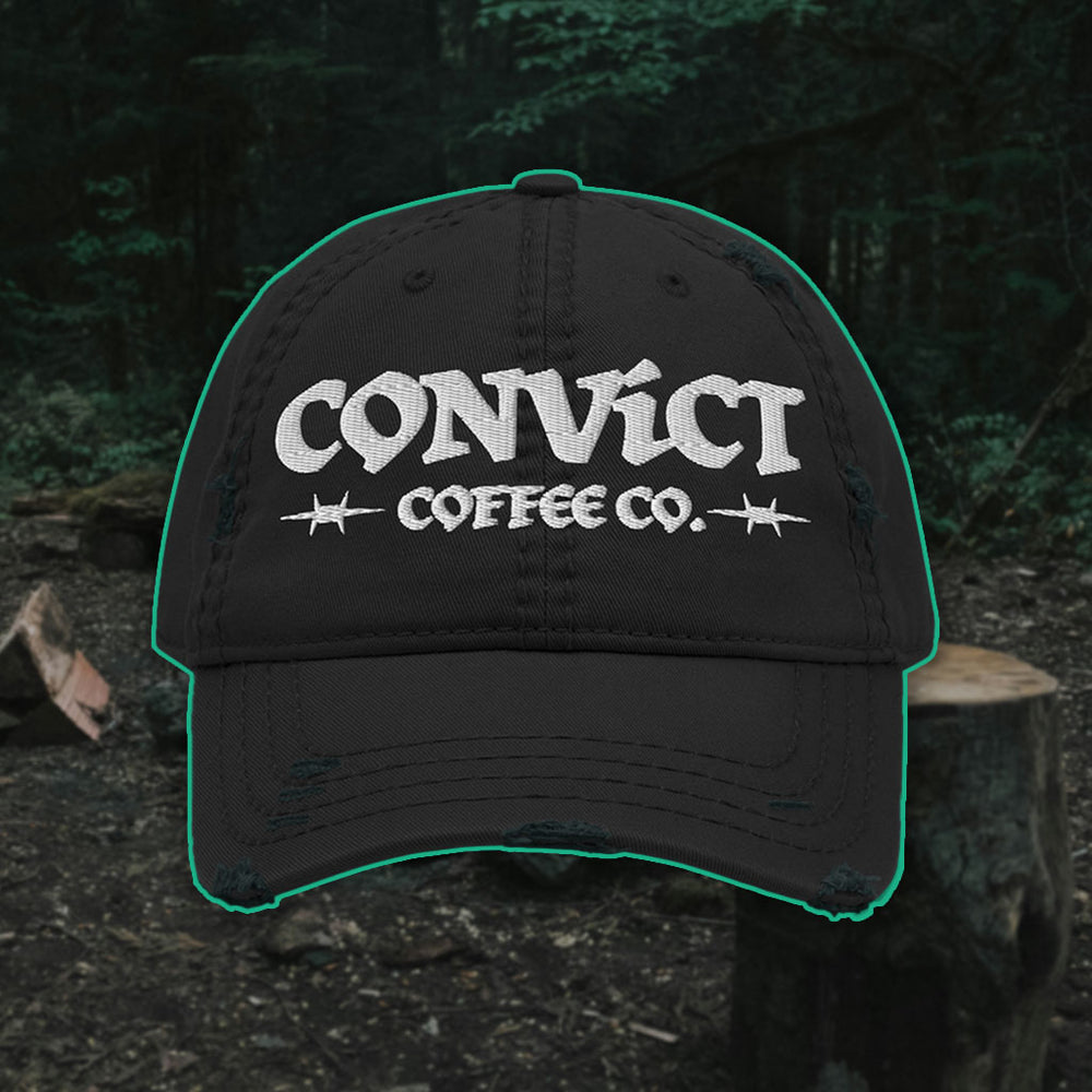 Black Distressed Dad Hat with 'Convict Coffee Co.' logo white embroidery on a Forest Campsite background with cut wood
