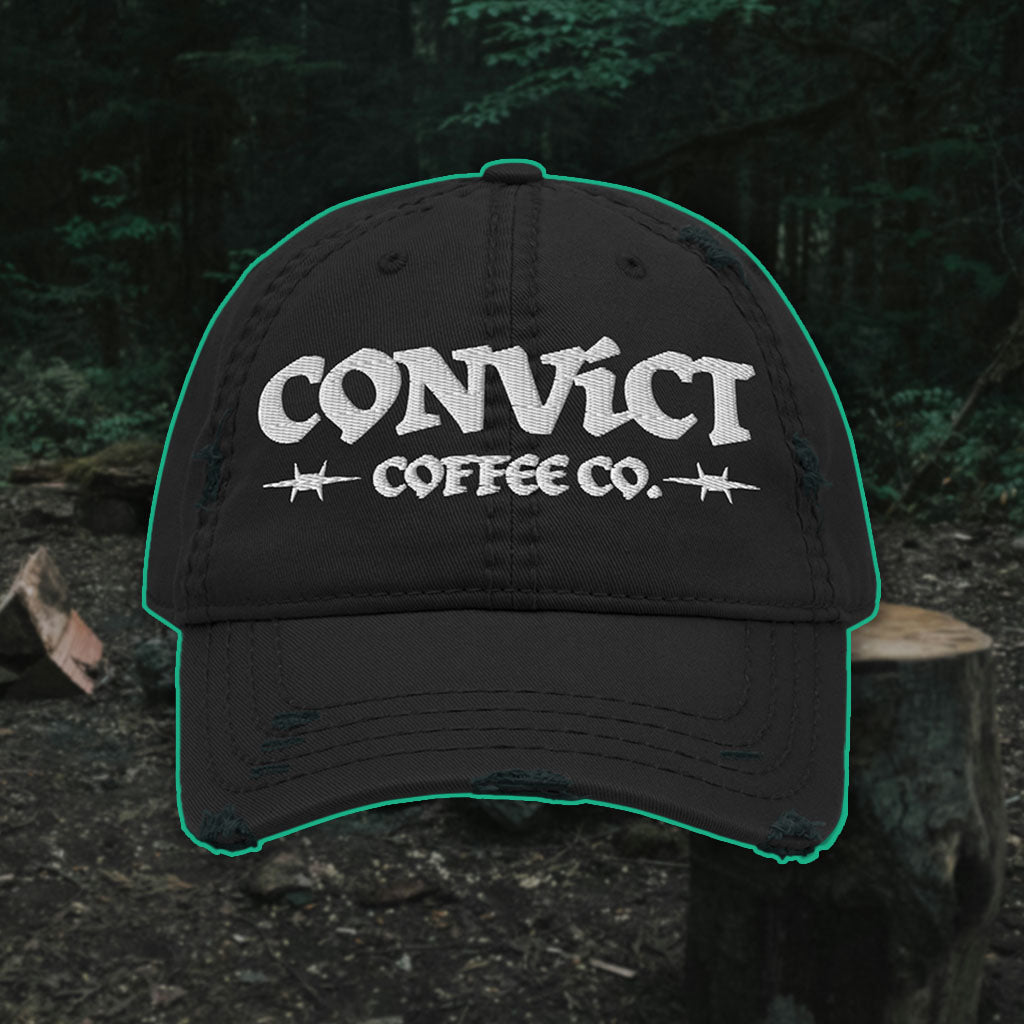 Black Distressed Dad Hat with 'Convict Coffee Co.' logo white embroidery on a Forest Campsite background with cut wood