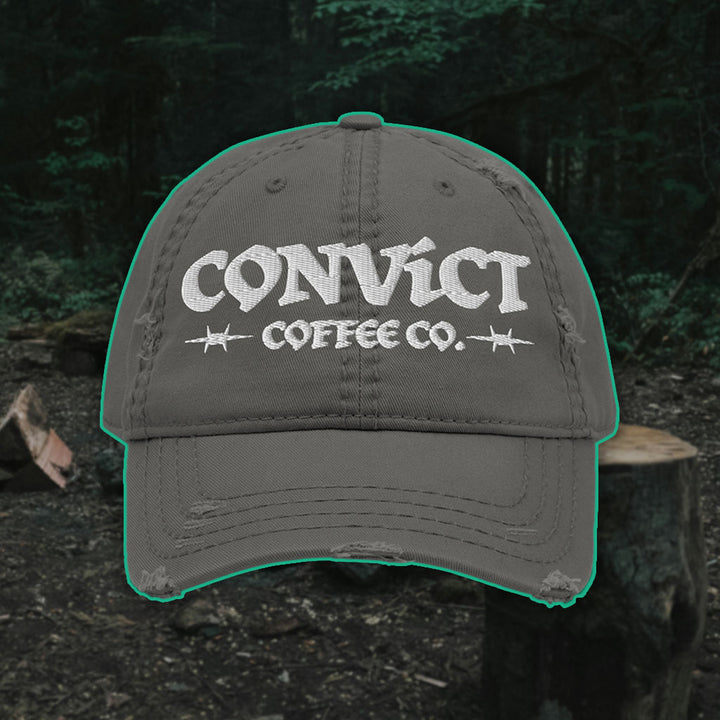 Charcoal Grey Distressed Dad Hat with 'Convict Coffee Co.' logo white embroidery on a Forest Campsite background with cut wood