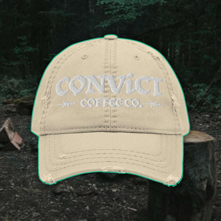 Khaki Distressed Dad Hat with 'Convict Coffee Co.' logo white embroidery on a Forest Campsite background with cut wood