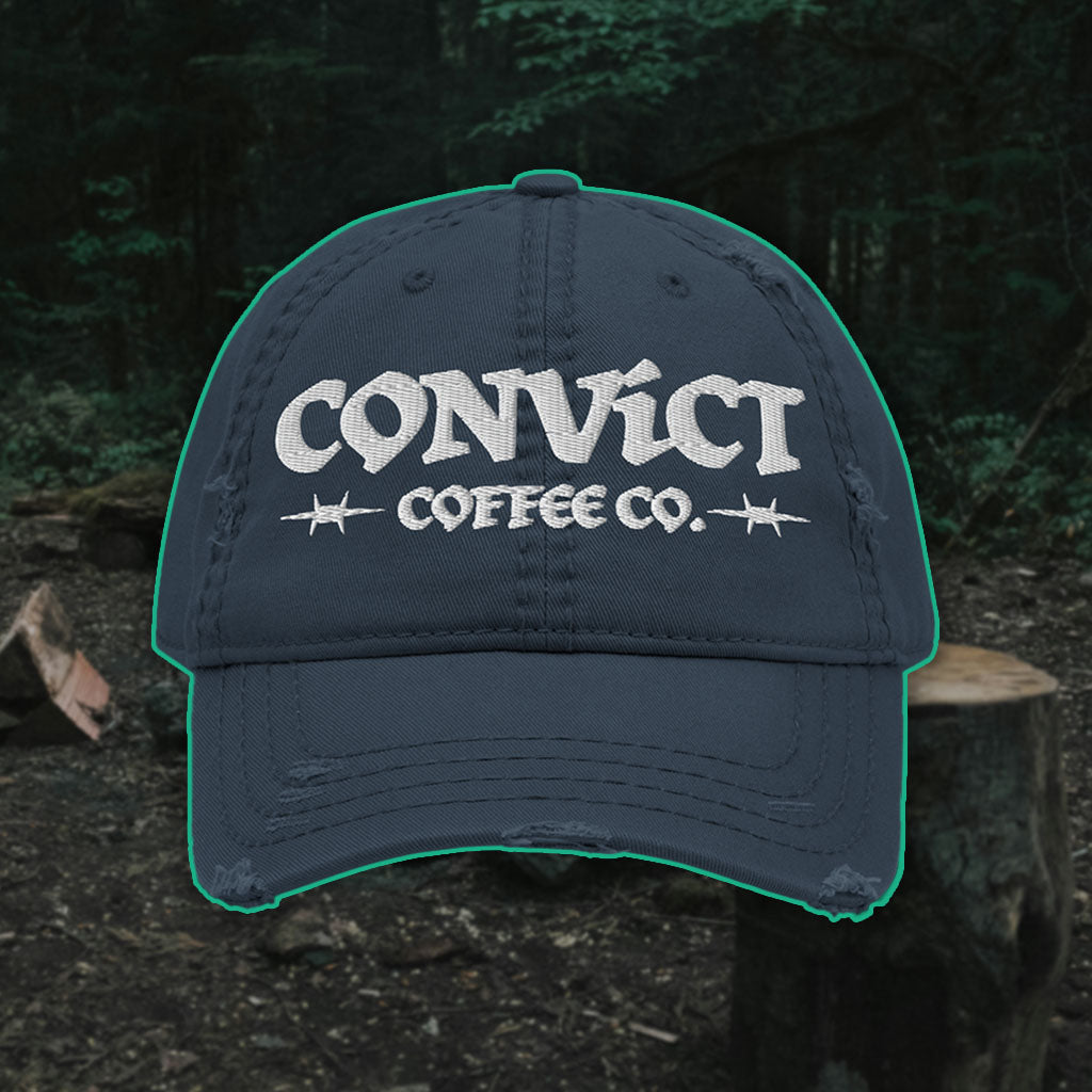 Navy Distressed Dad Hat with 'Convict Coffee Co.' logo white embroidery on a Forest Campsite background with cut wood