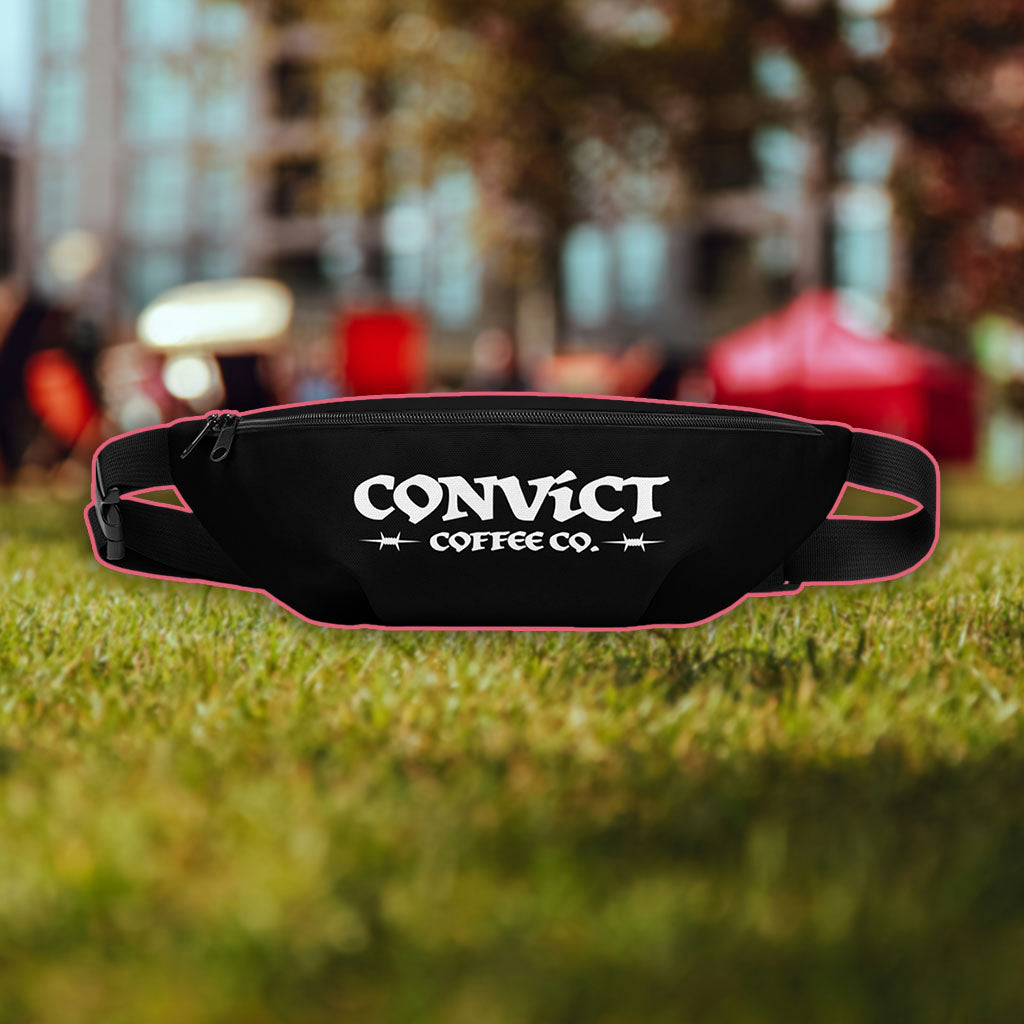 Fanny Pack with 'Convict Coffee Co.' branding white on black bag on grass background with tents and tall building