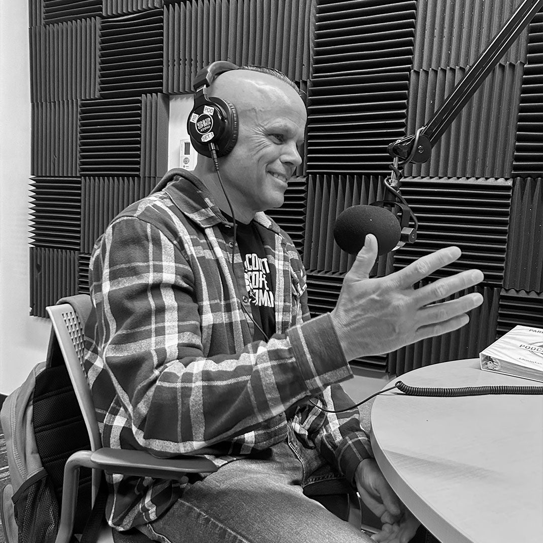Dan Klehm in a radio studio with headphones and microphone, surrounded by soundproofing panels black and white.