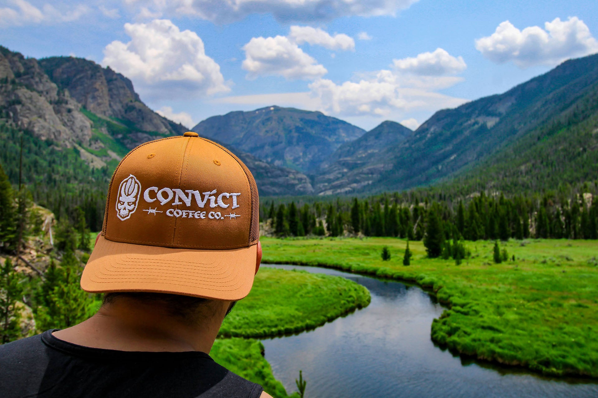 Person wearing a Caramel 'Convict Coffee Co.' cap with a scenic mountain landscape in the background