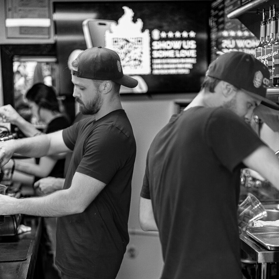 Daniel Klehm and Damien Klehm working behind a counter in a coffee shop black and white