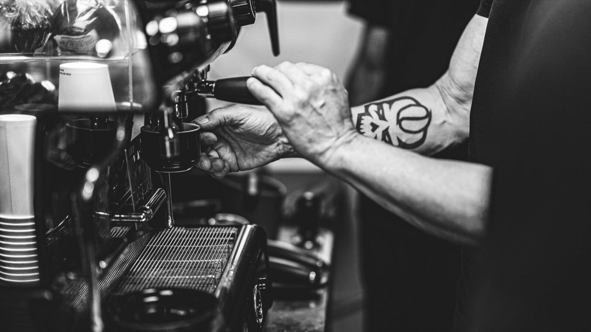 Person making coffee using a espresso machine with tattooed Convict Coffee Logo on Arm black and white