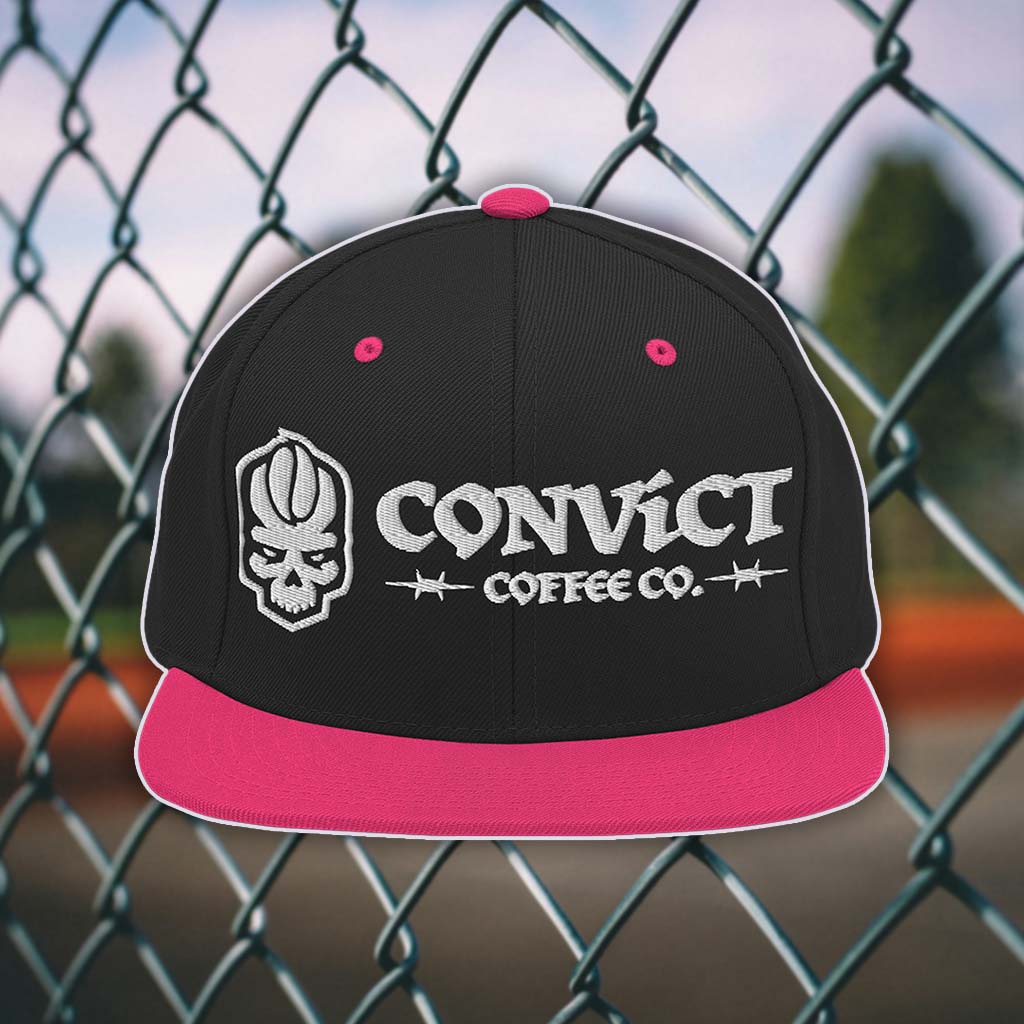 Black and Pink snapback flat bill with 'Convict Coffee Co.' logo white embroidery on a chain-link fence background