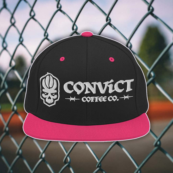 Black and Pink snapback flat bill with 'Convict Coffee Co.' logo white embroidery on a chain-link fence background