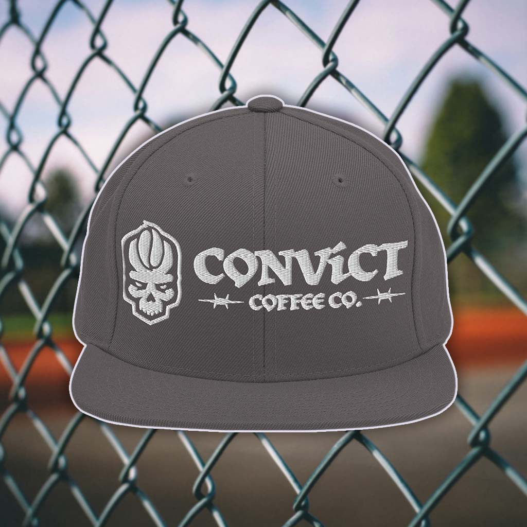 Dark Grey snapback flat bill with 'Convict Coffee Co.' logo white embroidery on a chain-link fence background