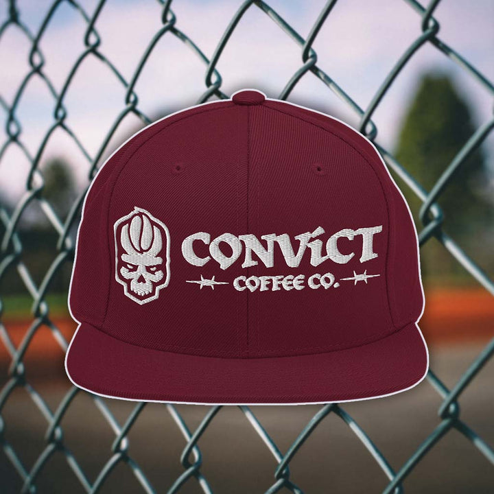Maroon snapback flat bill with 'Convict Coffee Co.' logo white embroidery on a chain-link fence background