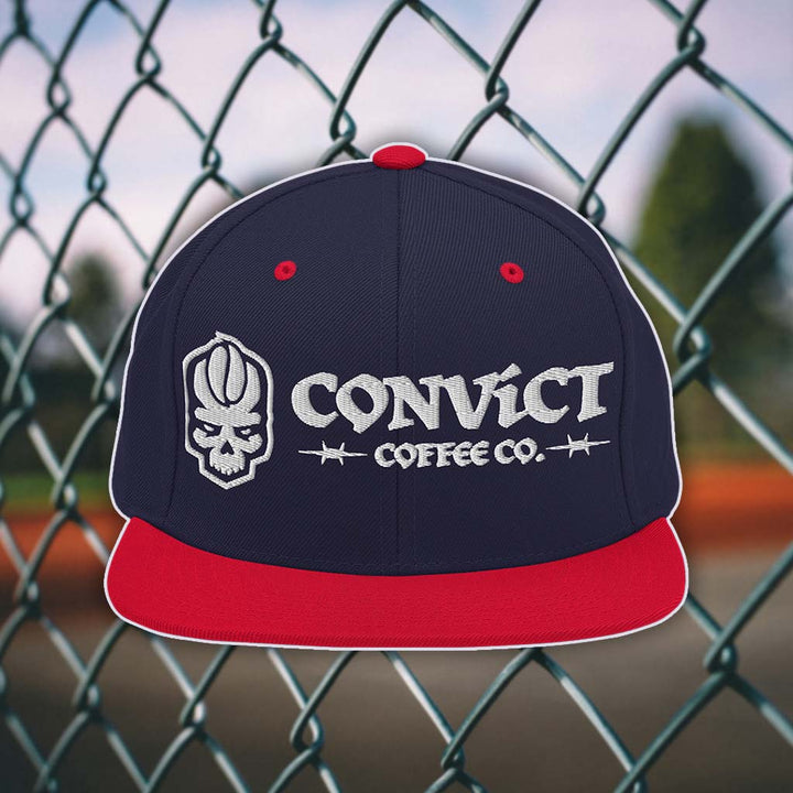 Navy and Red snapback flat bill with 'Convict Coffee Co.' logo white embroidery on a chain-link fence background