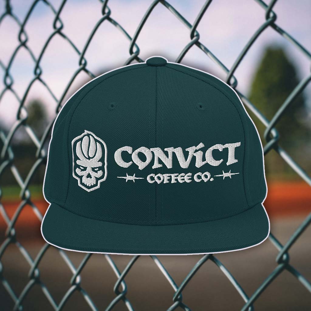 Spruce snapback flat bill with 'Convict Coffee Co.' logo white embroidery on a chain-link fence background