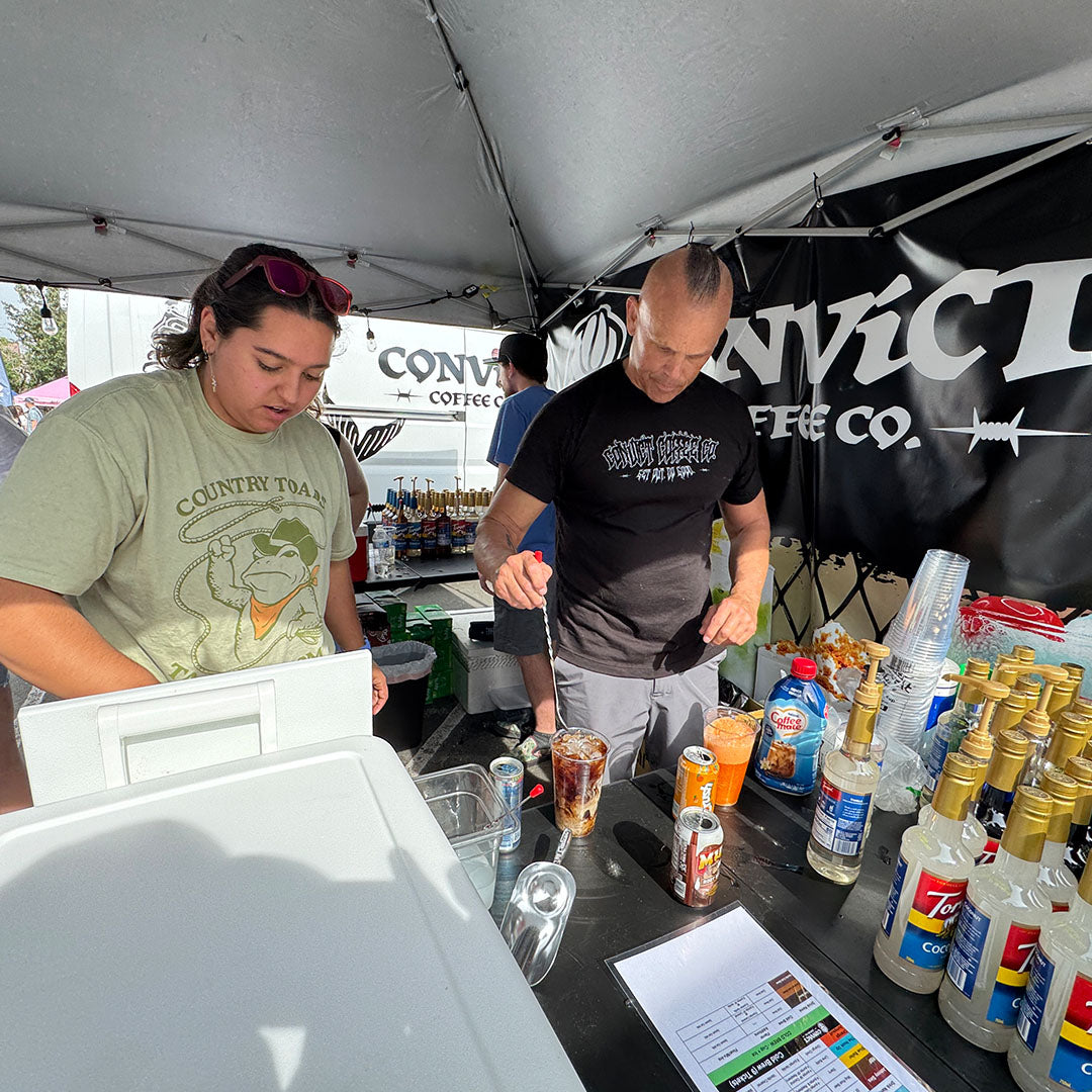 Dan Klehm and woman at a stand with various drinks and crafting a drink on a table under a tent.