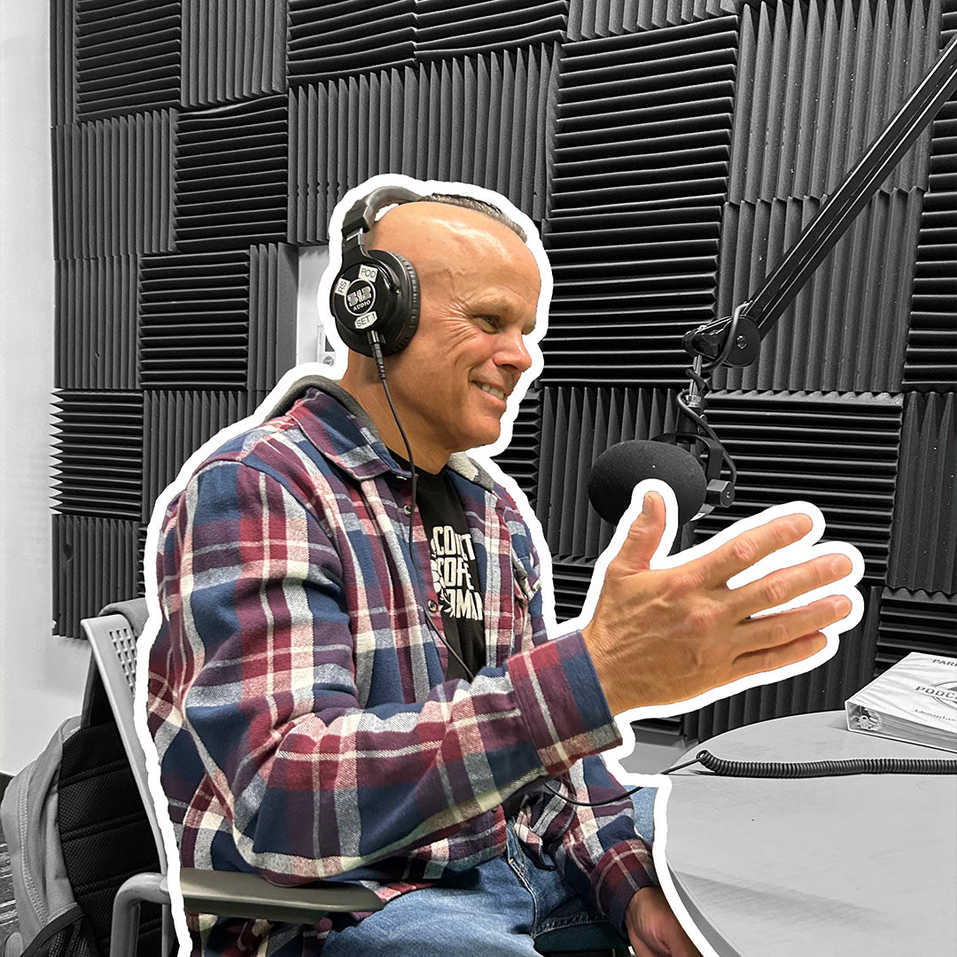Dan Klehm in a plaid shirt with headphones in a radio studio with soundproofing panels.