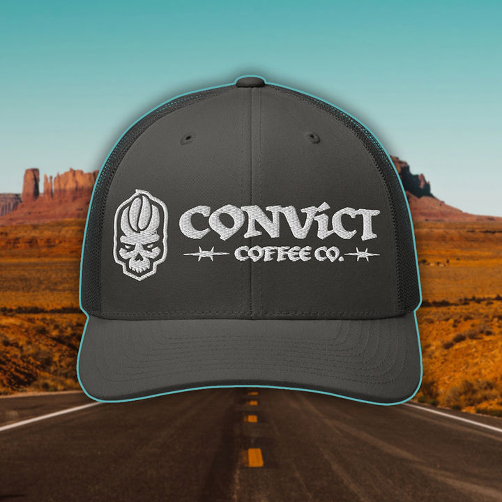 Charcoal Grey Trucker Hat with 'Convict Coffee Co.' logo white embroidery on a Desert Road background