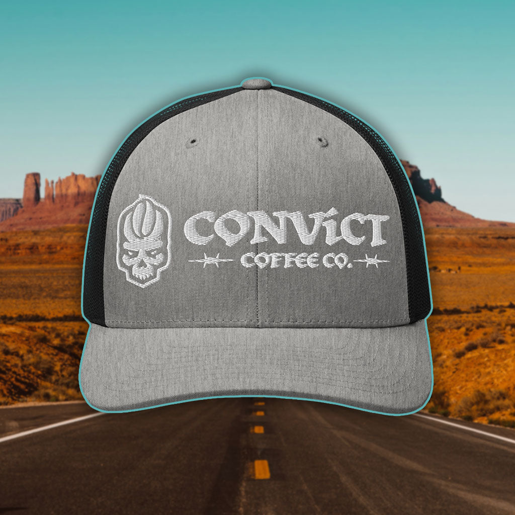 Heather Grey and Black Trucker Hat with 'Convict Coffee Co.' logo white embroidery on a Desert Road background