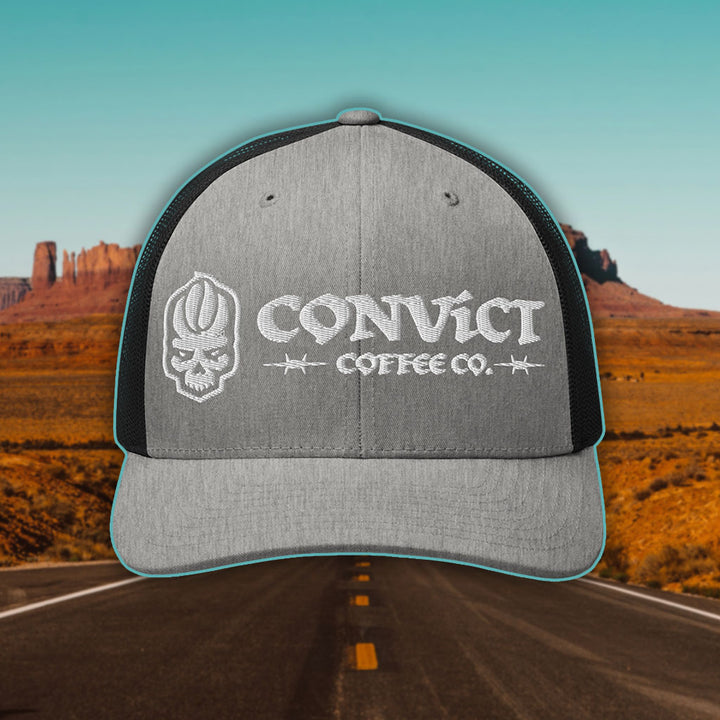 Heather Grey and Black Trucker Hat with 'Convict Coffee Co.' logo white embroidery on a Desert Road background