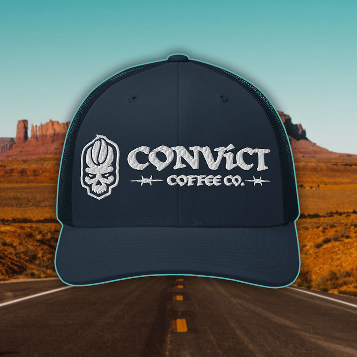 Navy Trucker Hat with 'Convict Coffee Co.' logo white embroidery on a Desert Road background